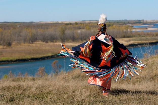 a woman in traditional dress looks out over a river and prairie