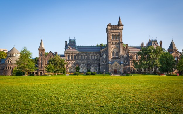 an old grey stone building sits behind a green field