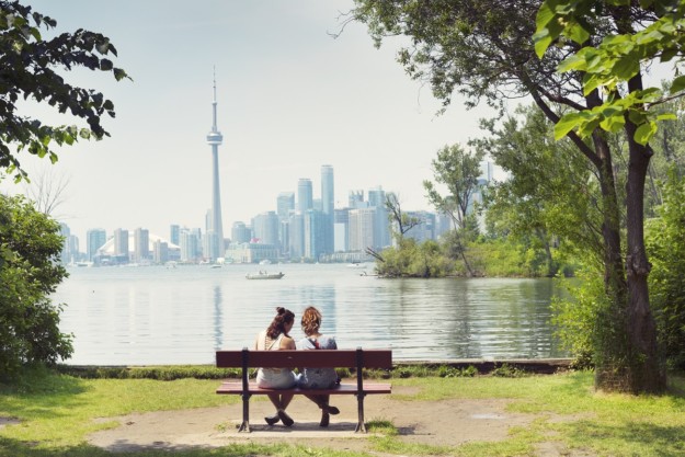 two people sit on a wooden bench looking out toward the Toronto cityscape
