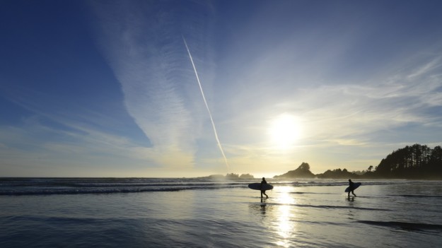 two surfers walk out to sea carrying their boards