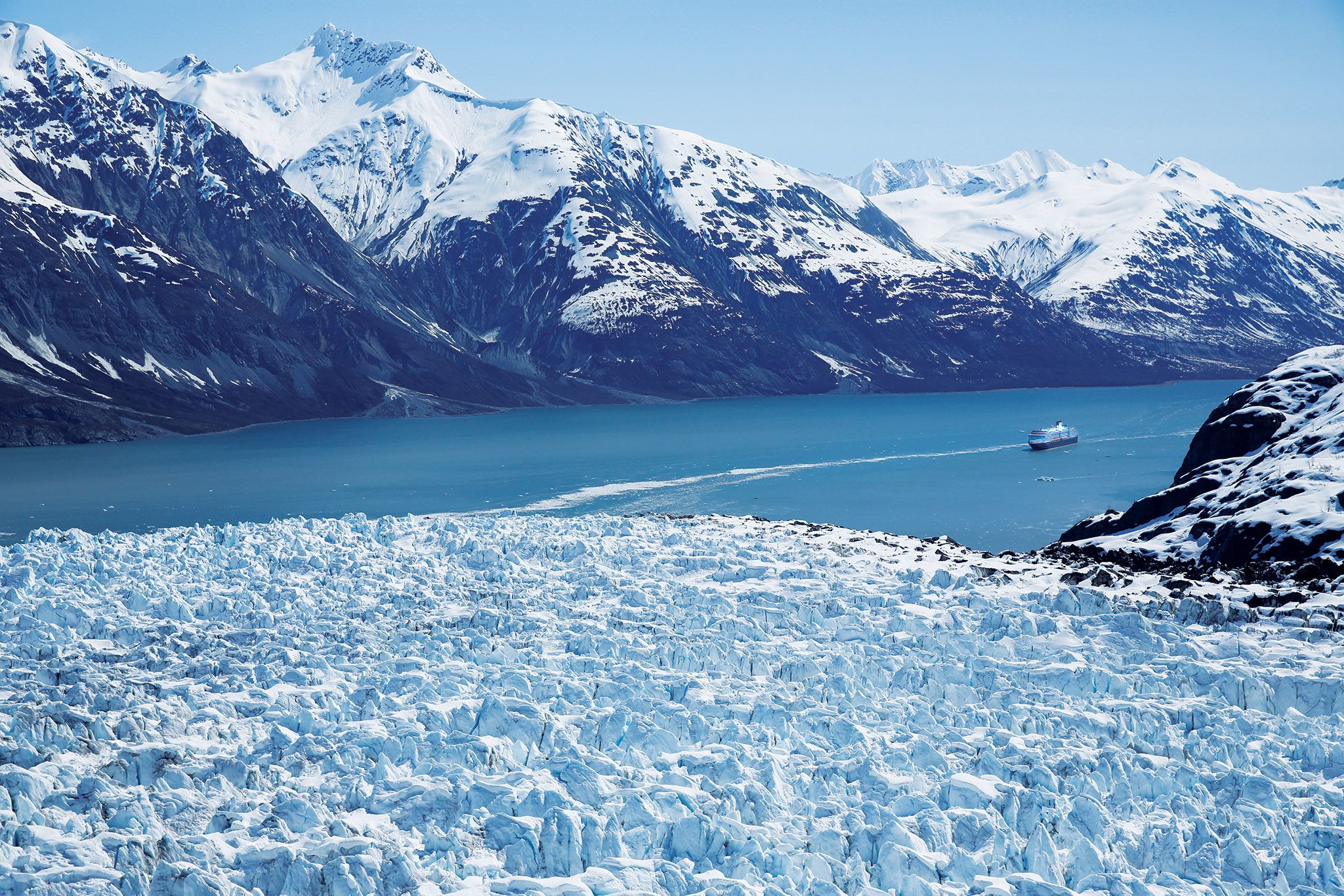 a cruise ship sails towards a giant glacier in the foreground
