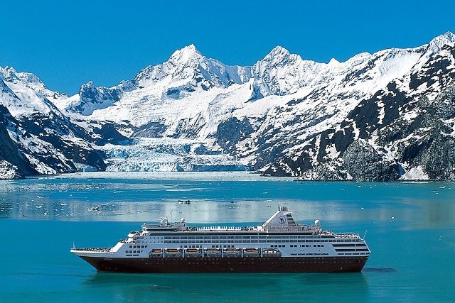 a cruise ship sits in the foreground with a glacier and mountains in the background