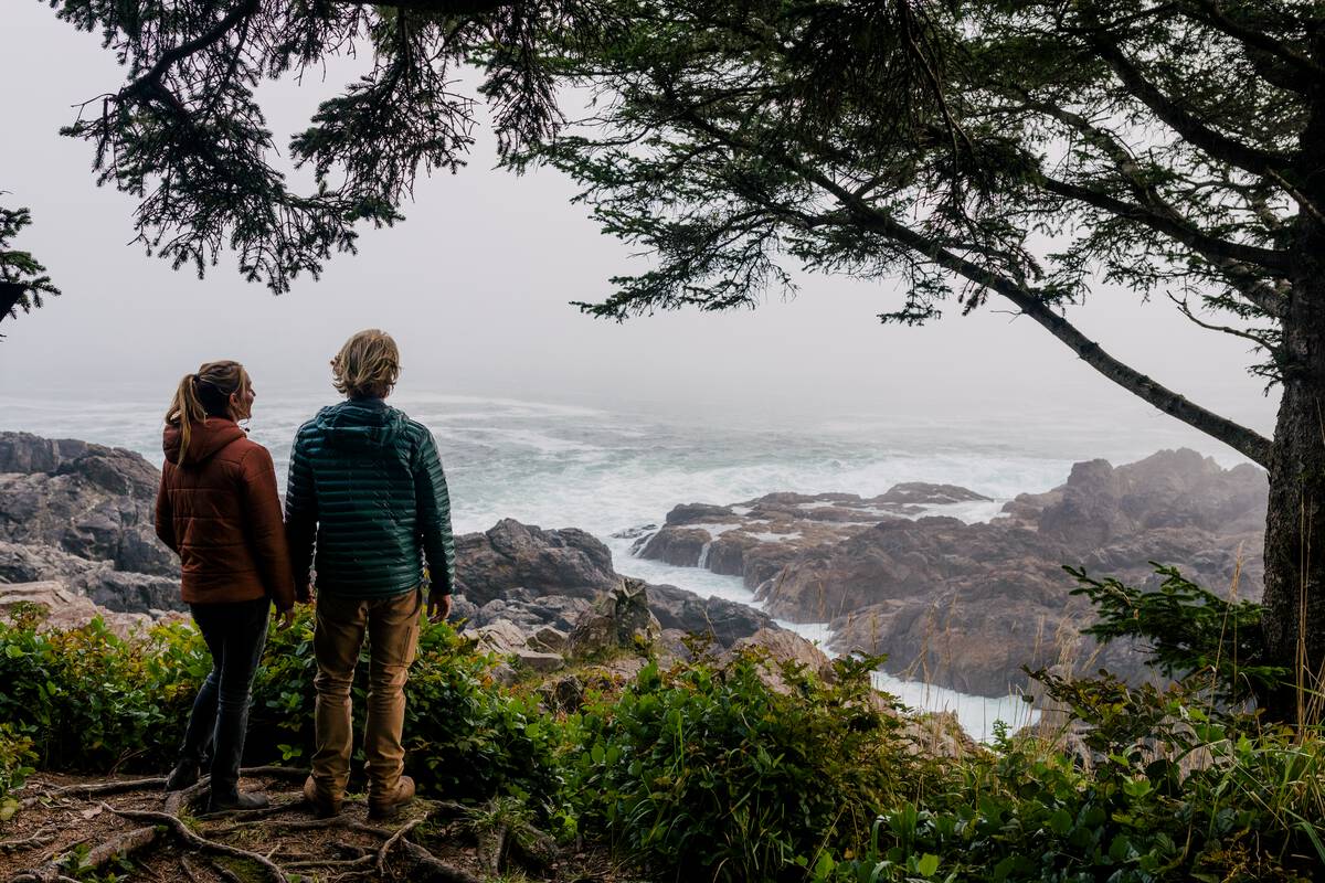 a couple of hikers take in the view of waves breaking on the shores of Pacific Rim National Park