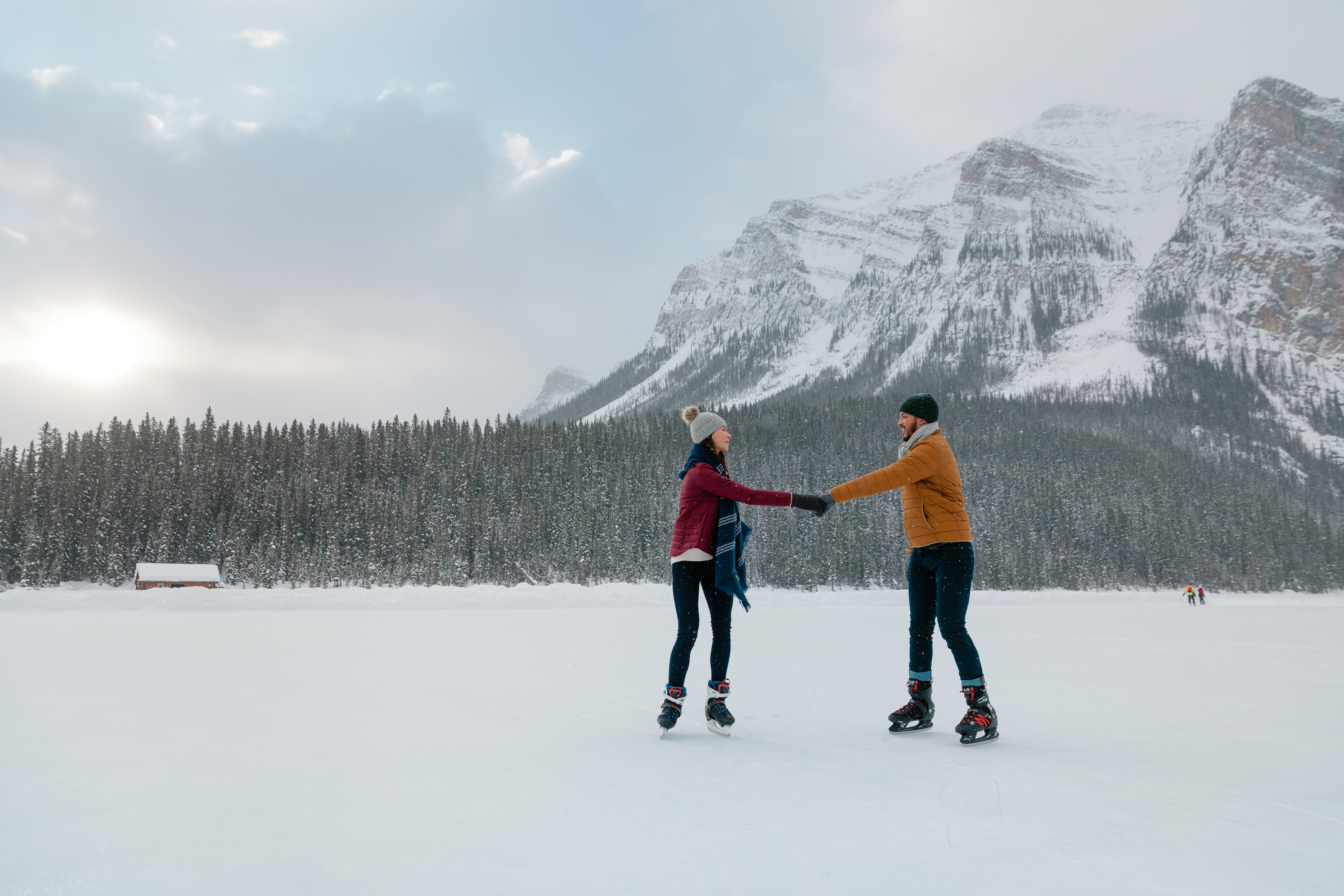 a couple ice skate on a forzen lake with a snowy mountain in the background