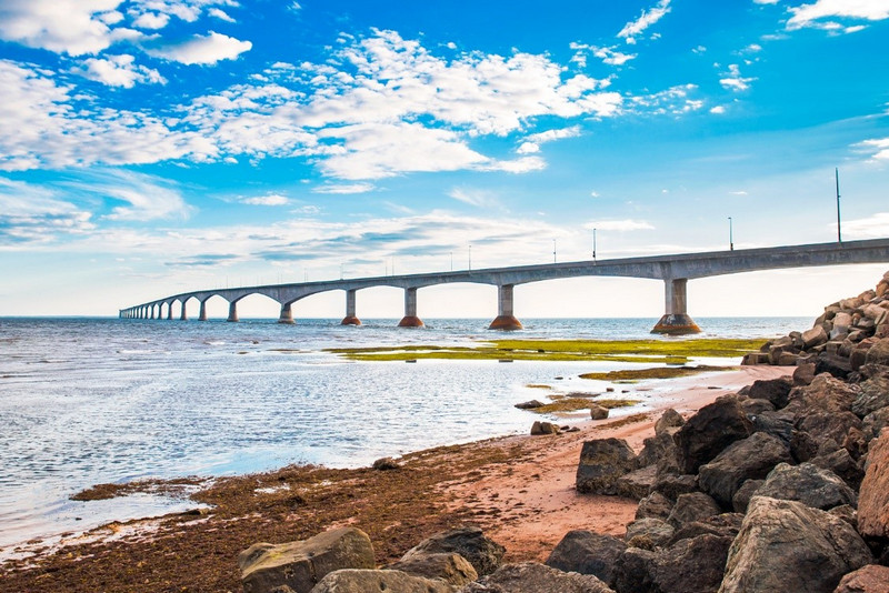 Confederation Bridge stretches out into the ocean with a small beach in the foreground