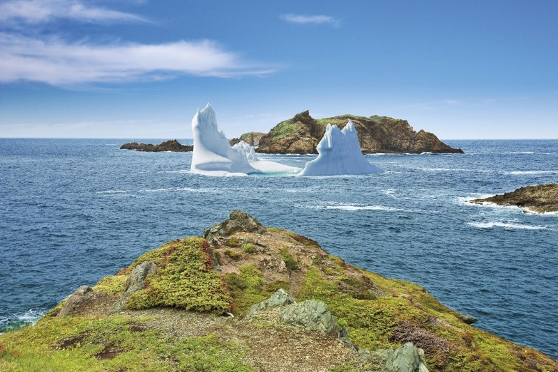 A scenic view of a historic stone tower on a rocky coastline in Nova Scotia under a wide sky with clouds, overlooking the ocean.