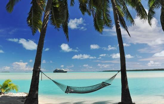A hammock between two palm trees on a sandy beach