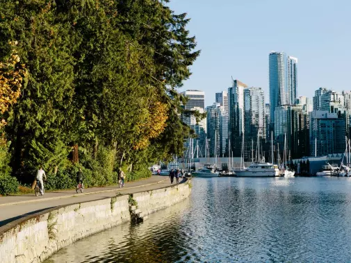 A scenic view of people walking and biking along Stanley Park sea wall, Vancouver  overlooking the marina filled with boats.
