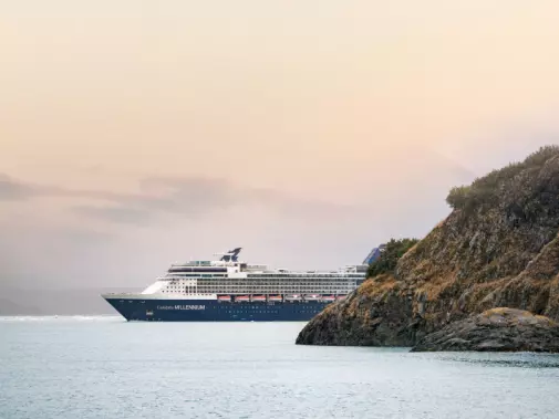 Sailing the Inside Passage rocky coastline under a soft, pastel-hued sunset sky during an Alaskan cruise.