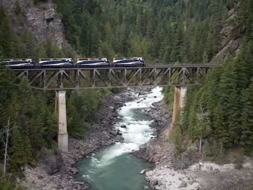  A  Rocky Mountaineer train journey across a towering bridge, nestled within a forested mountain valley.