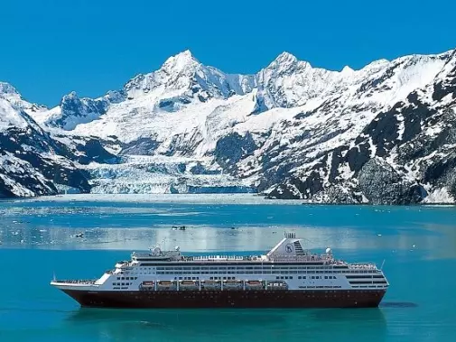 A cruise ship sails in The clear blue waters of a stunning Glacier Bay with snow-capped mountains under a bright blue sky.