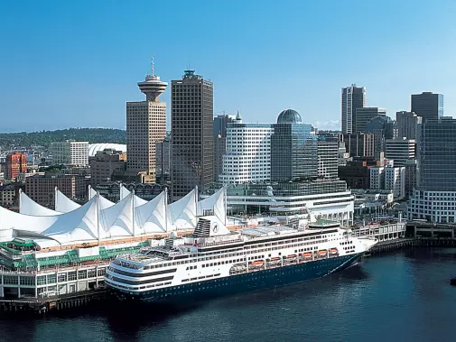 A sunny view of Vancouver city skyline featuring modern buildings, and Holland America Line cruise ship docked at the waterfront.